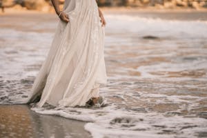 A bride wades through gentle surf in an elegant wedding dress at the beach.