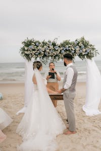 Elegant beachside wedding with a flower-adorned arch and officiant, capturing love by the sea.